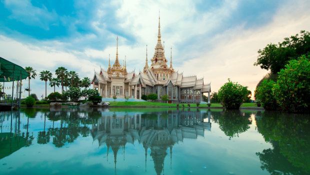 Thai temple reflected in calm green water surrounded by lush scenery