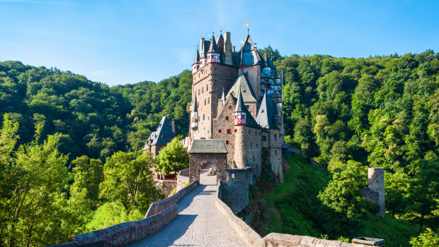 Burg Eltz Castle hidden among lush green forests in the Moselle Valley, Germany, with a stone path leading to the gate.