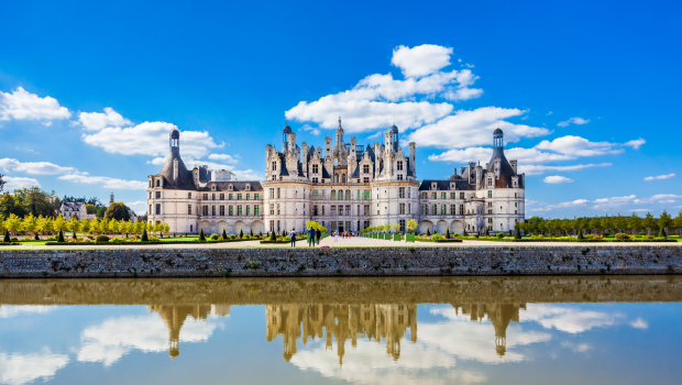 Château de Chambord in the Loire Valley, France, with perfect reflection on a calm pond under a bright blue sky.