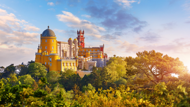 Colorful Pena Palace in Sintra, Portugal, standing on a hilltop among forests and mountains at sunset.
