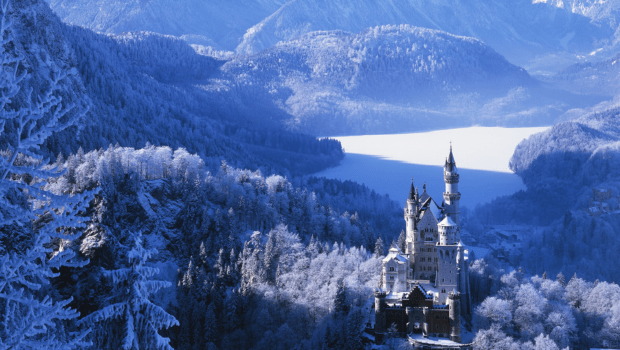 Neuschwanstein Castle surrounded by snowy Bavarian mountains and a frozen lake in southern Germany