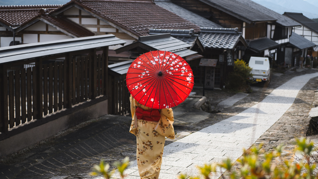 Woman in traditional kimono walking with a red umbrella in a Japanese village