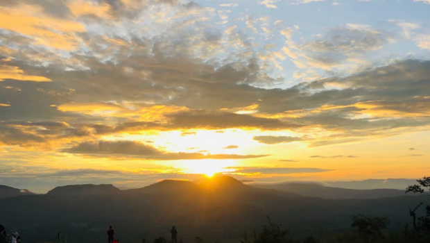 sun rising behind mountain ridges with glowing clouds