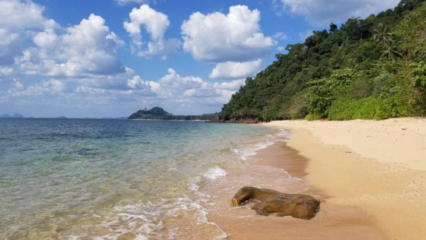 clear water, soft sand, green hillside, bright sky