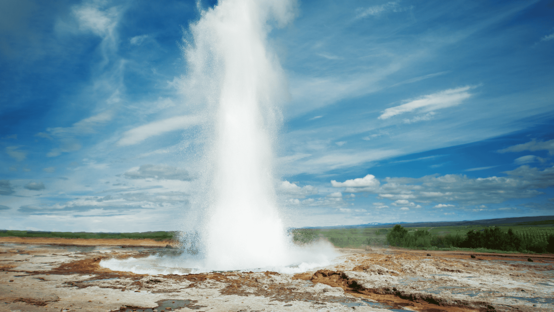 น้ำพุร้อน Geysir ในไอซ์แลนด์พ่นน้ำร้อนขึ้นสู่ท้องฟ้าอย่างทรงพลัง ท่ามกลางท้องฟ้าสีฟ้าสดและเมฆลอยตัว