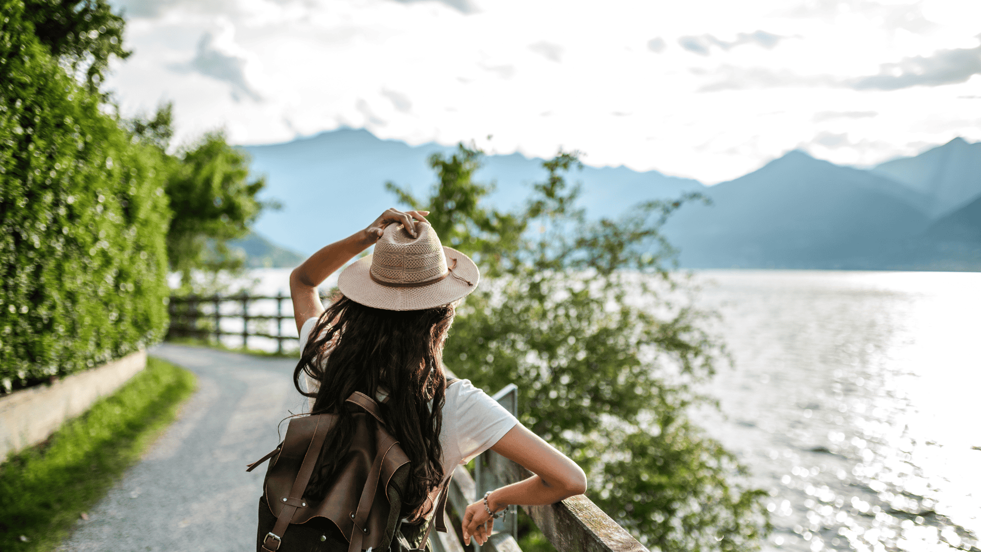 ผู้หญิงสะพายเป้เดินชมวิวริมทะเลสาบใส มีฉากหลังเป็นเทือกเขาสูงและเส้นทางธรรมชาติร่มรื่น