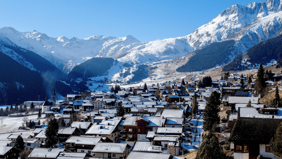 Snow-covered alpine village surrounded by mountains under a clear blue sky in Europe