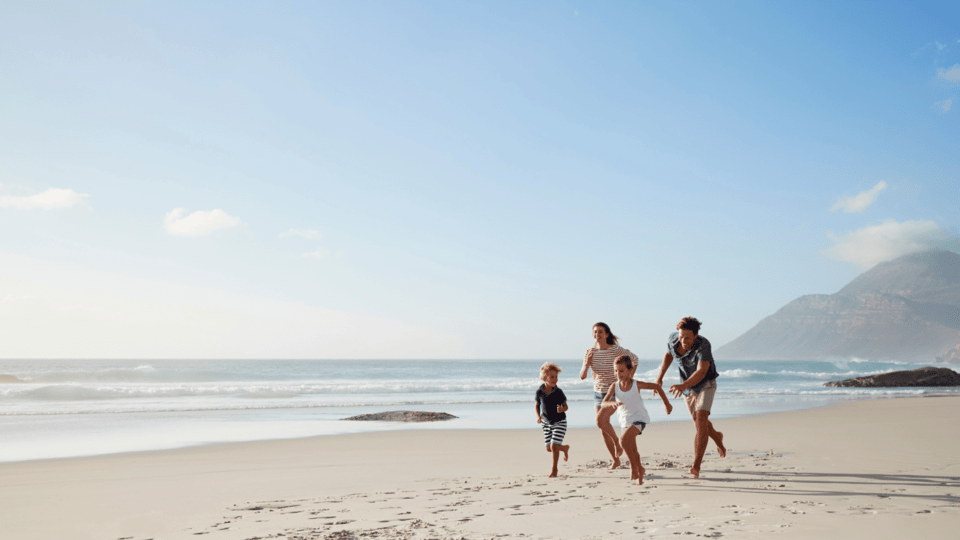 A family running and playing together on a sandy beach with the ocean and mountains in the background on a sunny day