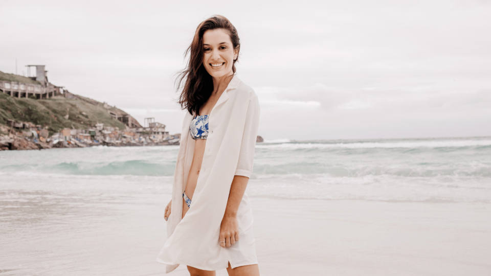 A woman smiling while walking along the beach with ocean waves behind her on a cloudy day