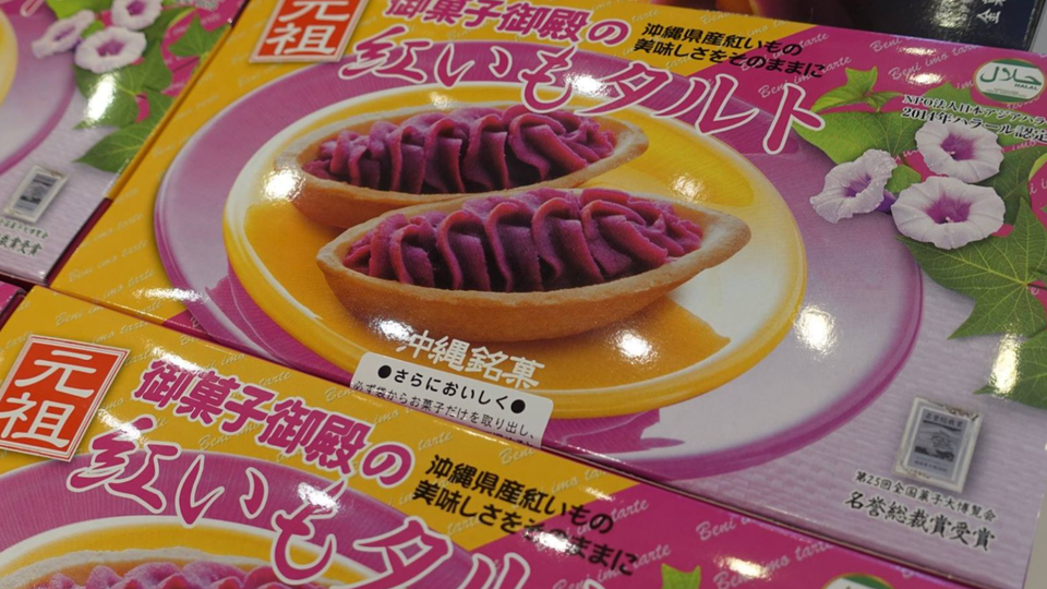 Brightly packaged Okinawan beni imo (purple sweet potato) tarts displayed in pink and yellow boxes, showing the vivid purple filling inside golden pastry shells.