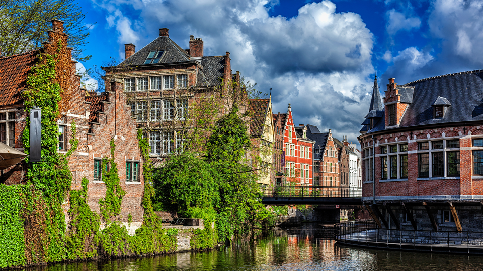 Scenic view of Girona Old Town, Spain, with historic fortress walls on a hill, terracotta rooftops, and lush green cypress trees in a peaceful setting.