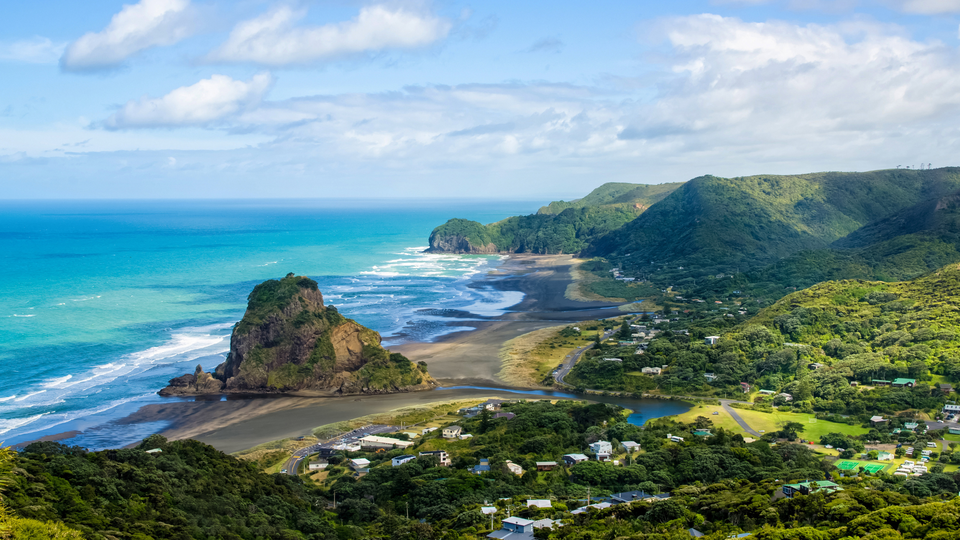 Coastal landscape of Napier, New Zealand, with turquoise ocean waves, a rocky headland, and green hills overlooking a quiet seaside town.