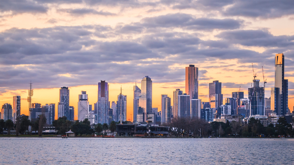 Melbourne skyline at sunset viewed across the river, featuring modern skyscrapers, calm water, and warm evening light.