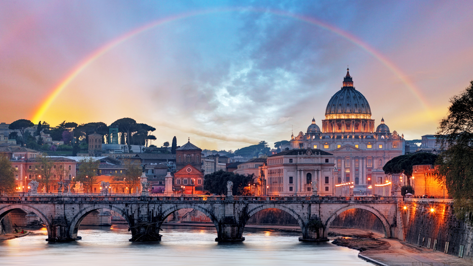 Rainbow over St. Peter’s Basilica in Rome at sunset with historic bridges and the Tiber River in the foreground.