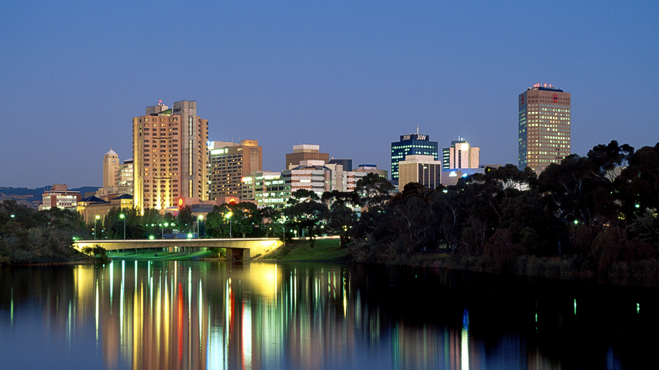 Adelaide city skyline at night reflected in the River Torrens with illuminated buildings and bridge.