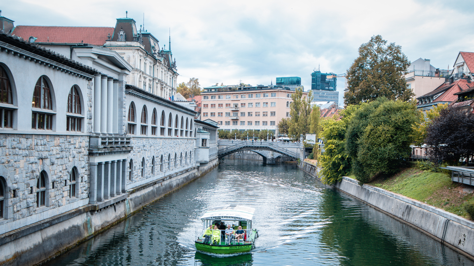 Tour boat cruising along the Ljubljanica River with historic architecture and bridge in Ljubljana old town.