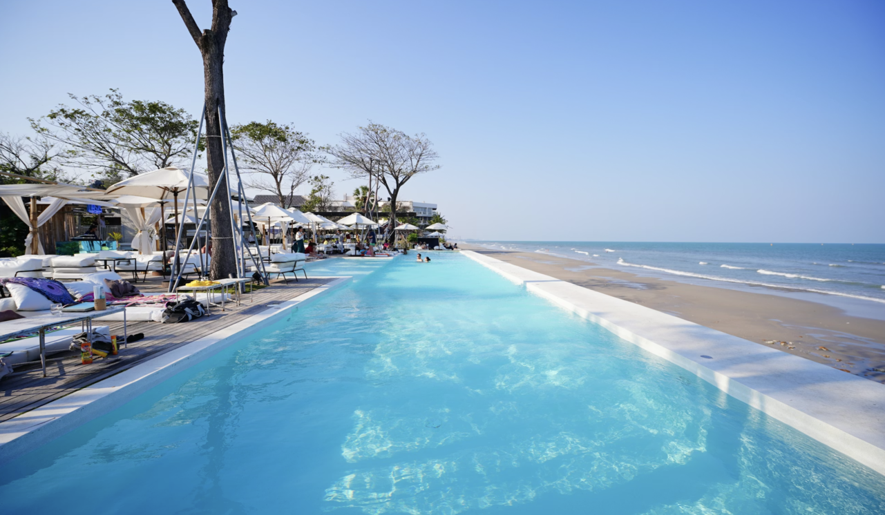 Colorful sunset over Hua Hin beach with waves, rocky shoreline, and silhouettes of people watching the evening sky.