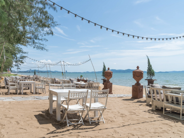 Beachfront café seating with white tables and chairs on the sand overlooking the sea in Hua Hin, Thailand, with string lights and coastal views.